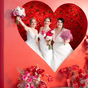 Bräute in der Fotospot Herz-Wall. Rote Flowerwall mit riesigem Herz