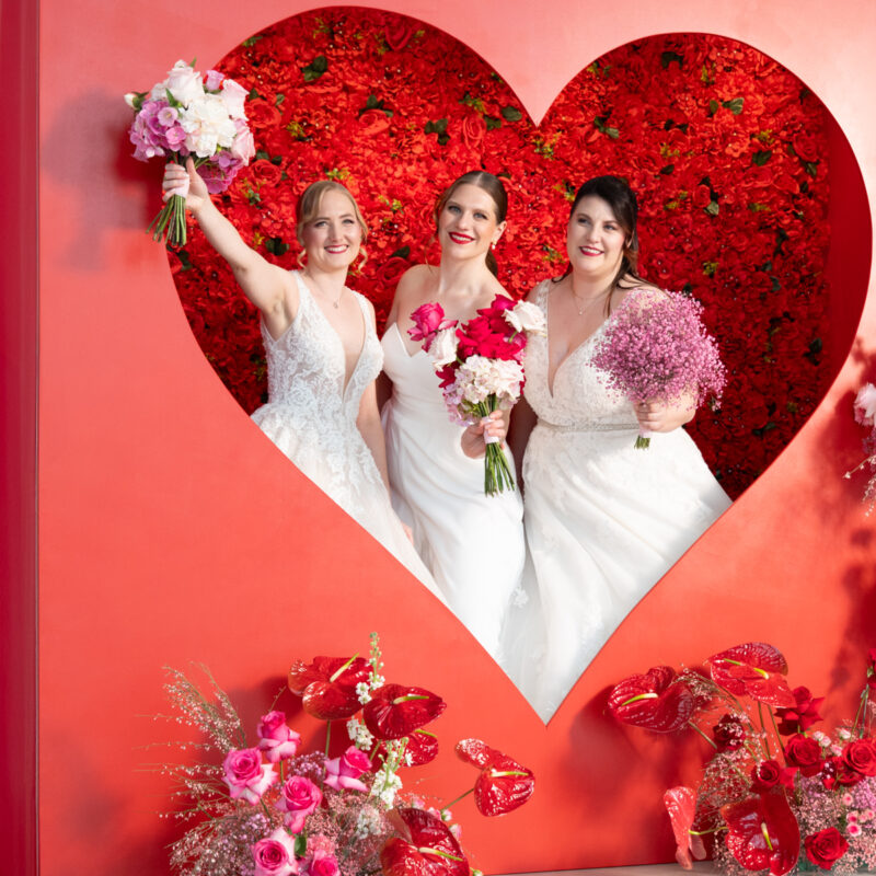 Bräute in der Fotospot Herz-Wall. Rote Flowerwall mit riesigem Herz